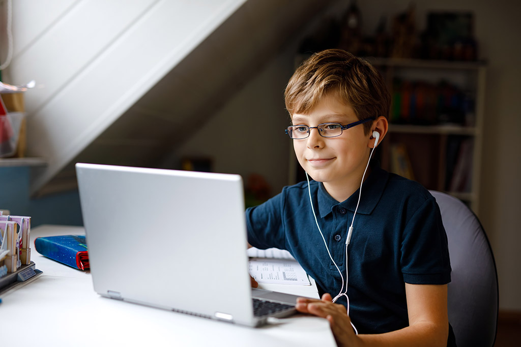 Kid boy with glasses learning at home on laptop for school. Adorable child making homework and using notebook and modern gadgets. Home schooling concept.